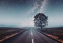 Een eenzame weg die leidt naar een heldere sterrenhemel met de Melkweg en een boom langs de weg, symbool voor spirituele groei en astrologie.