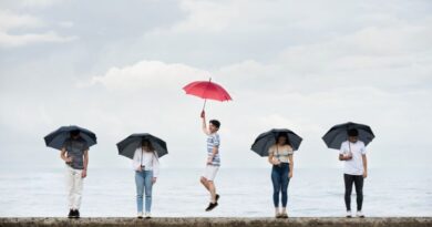 A young man jumps joyfully holding a vibrant red umbrella while surrounded by four somber people holding black umbrellas against a cloudy coastal backdrop, symbolizing the breakthrough of existential depression.