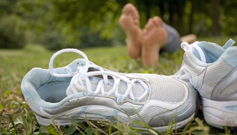 A pair of light blue running shoes in the grass with a person resting in the blurred background, enjoying nature. Stop-procrastinating.