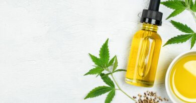 Hennepolie in een pipetflesje omringd door cannabis bladeren en hennepzaden op een witte achtergrond.