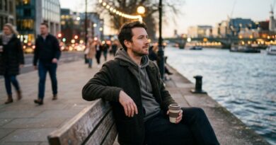 A thoughtful man sitting on a park bench by a river in a busy city, illustrating a highly sensitive person (HSP) managing sensory input and emotional intensity.