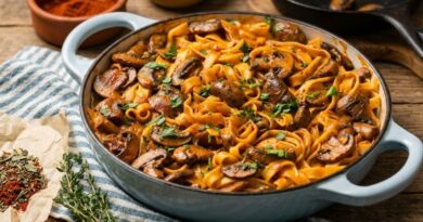 Close-up photo of a rustic blue enameled skillet filled with creamy Cajun mushroom pasta and tagliatelle on a wooden table. The dish is garnished with fresh parsley and surrounded by bowls of smoked paprika and herbs.