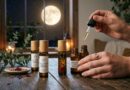Hand die etherische olie druppelt in een glazen rollerflesje op een houten tafel, met op de achtergrond een volle maan door het raam