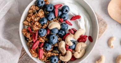 Bovenaanzicht van een gezonde ontbijtkom met granola, Griekse yoghurt, verse blauwe bessen, rode goji-bessen en cashewnoten. Een ideale balans van vezels en probiotica voor darmgezondheid.