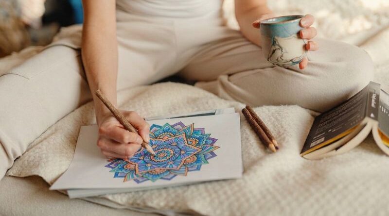 A person sitting comfortably, holding a warm drink while coloring an intricate geometric mandala with colored pencils for stress relief and relaxation.