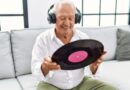 Glimmlachende oudere man luistert naar muziek met koptelefoon en vinylplaat