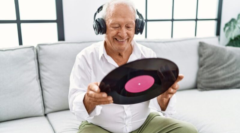 Glimmlachende oudere man luistert naar muziek met koptelefoon en vinylplaat