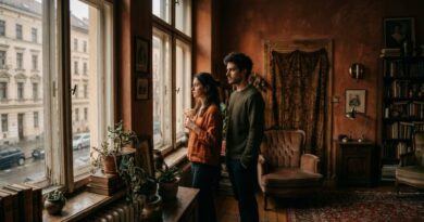 A moody cinematic lifestyle photograph of a man and a woman standing near a window with soft natural light, looking in different directions to convey emotional distance.
