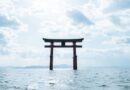 A traditional Japanese torii gate standing in the middle of a calm ocean under a bright, cloudy sky, representing spiritual presence and nonduality.