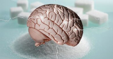 An anatomical model of a human brain sitting on top of a mound of white granulated sugar, surrounded by blurred sugar cubes and static electricity or lightning effects on a light blue background.