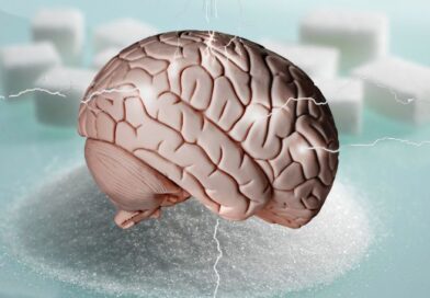 An anatomical model of a human brain sitting on top of a mound of white granulated sugar, surrounded by blurred sugar cubes and static electricity or lightning effects on a light blue background.