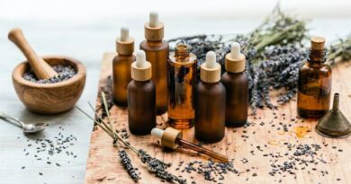 A rustic wooden table with amber glass dropper bottles filled with homemade lavender infused oil, surrounded by dried lavender flowers, a mortar and pestle, and a small funnel.