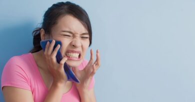 Een jonge vrouw in een roze shirt drukt pijnlijk kijkend een blauw koelkompres tegen haar rechterkaak vanwege hinderlijke mondpijn of tandpijn.